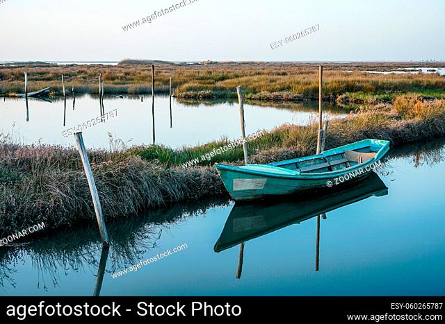 Horizontal photo of a weathered and abandoned small boat close to shore in peaceful lagoon on bright day