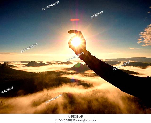 Man hand touch Sun. Misty daybreak in a beautiful hills. Peaks of hills are sticking out from foggy background, the fog is red and orange due to Sun rays
