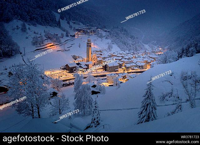 Winter dusk over the illuminated village in deep snow, Gerola Alta, Valgerola, Orobie Alps, Valtellina, Lombardy, Italy, Europe