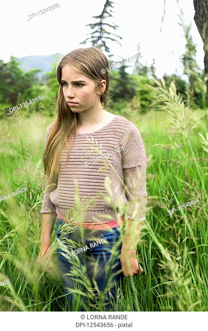 A preteen girl stands in tall grass in a field; Salmon Arm, British Columbia, Canada