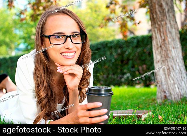 portrait of a young attractive woman in the park with a paper glass of coffee. Rest in the park
