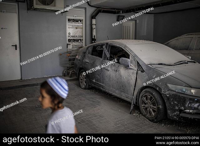 14 May 2021, Israel, Ashkelon: A child stands in front of destroyed cars in a garage at a house that was hit by a rocket fired from the Gaza Strip towards...