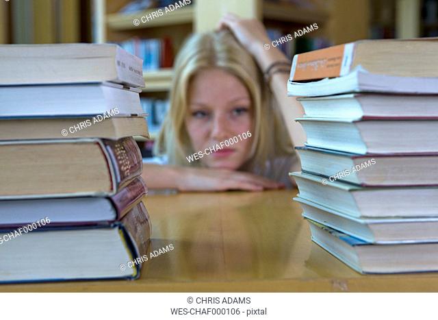 Germany, Baden-Wuertemberg, stressed young female student with stack of books in a library