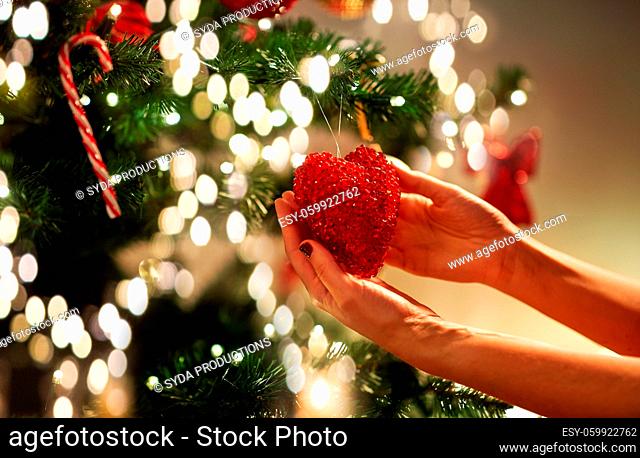 hands decorating christmas tree with red heart