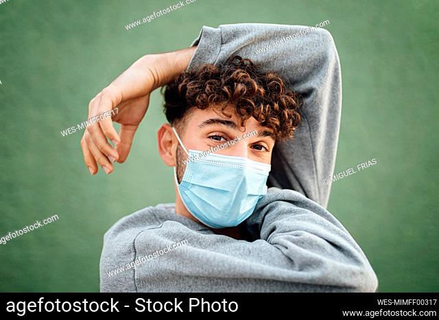Man with hand raised wearing surgical mask against green background in studio