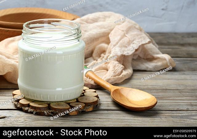 homemade yogurt in a glass transparent jar on a wooden table, a healthy fermented milk product