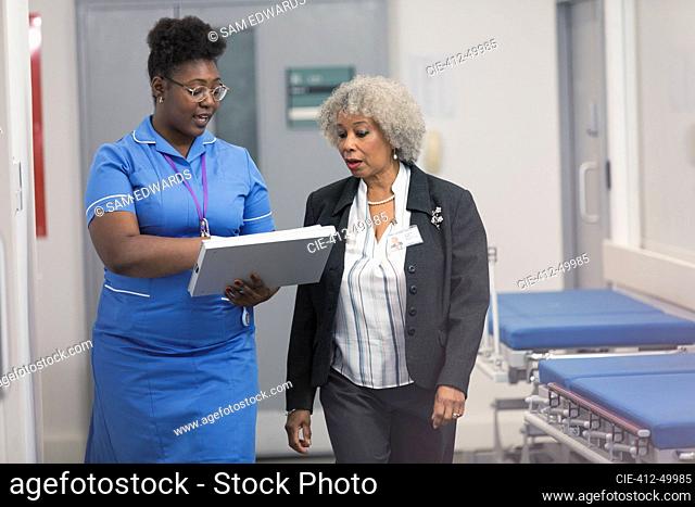 Female doctor and nurse discussing medical chart, making rounds in hospital corridor