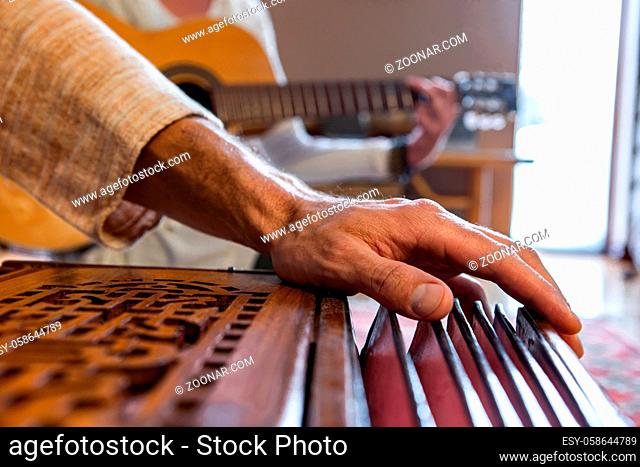 Closeup of senior hands playing indian classical sacred kirtan music for silence and peace using harmonium with woman playing classical guitar