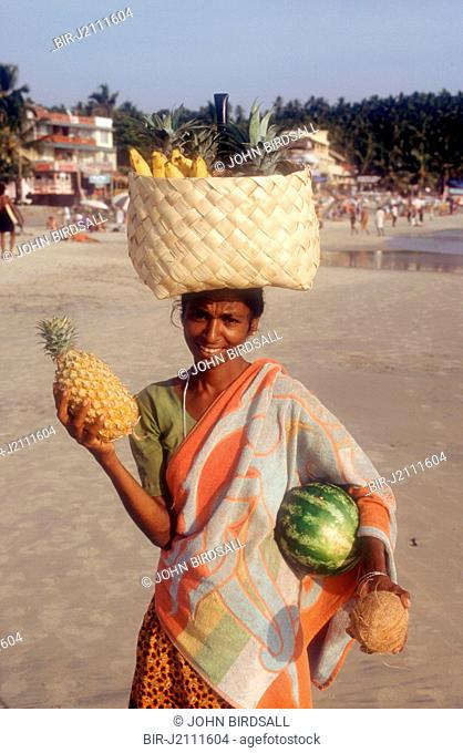 Fruit seller and tourists on the beach at Kovalam beach, Kerala, India