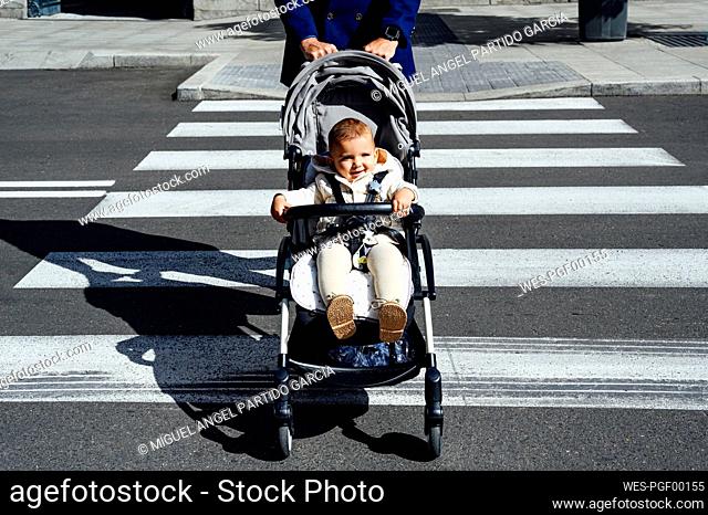 Father with smiling baby in baby stroller crossing road in city