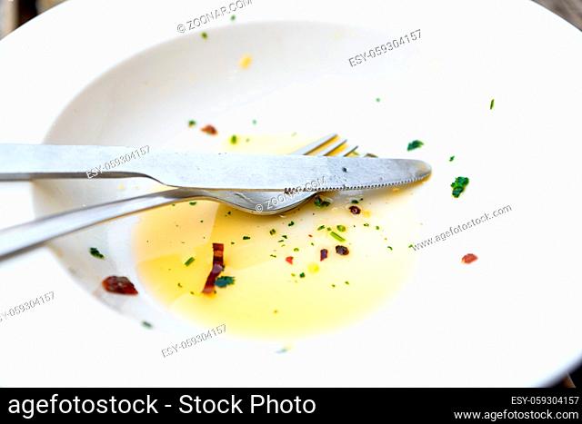 Empty white plate, knife and fork with olive oil, herbs and chili flakes leftover