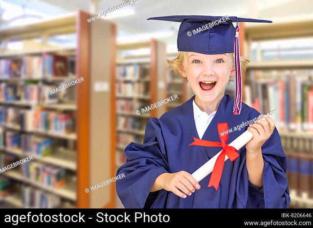 Cute young caucasian boy wearing graduation cap and gown in the library