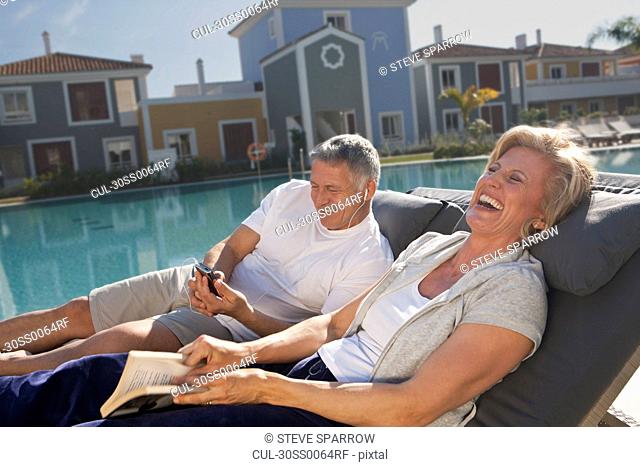 Couple on sunbeds laughing by pool
