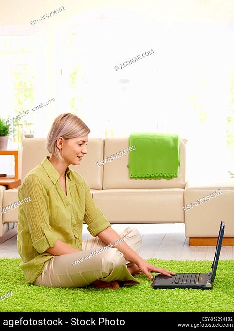 Attractive woman sitting on floor in living room looking at laptop