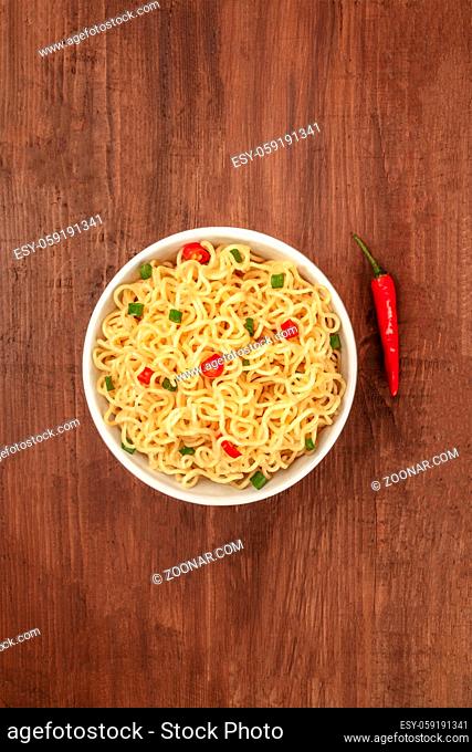 An overhead photo of a bowl of noodles with a red hot chili pepper and copy space, on a dark rustic background texture