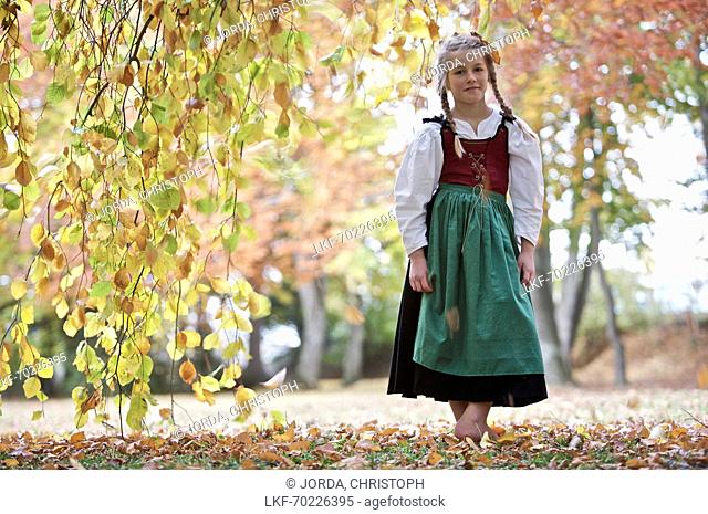 A girl wearing a Dirndl dress standing below a tree, Kaufbeuren, Bavaria, Germany