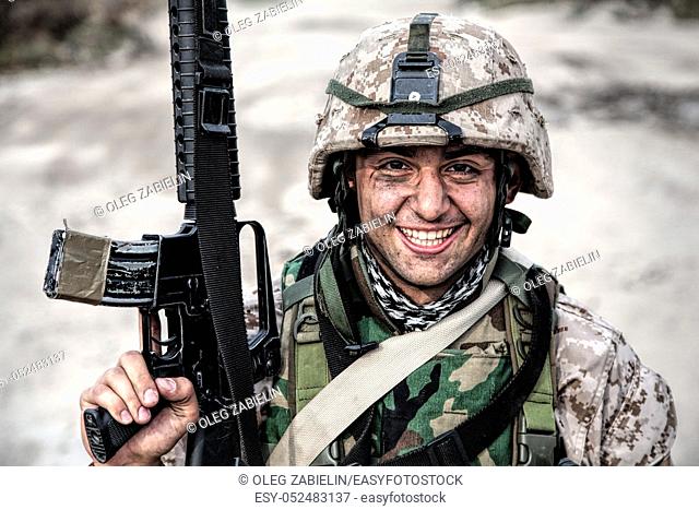 Smiling army soldier, United States Marine Corps infantry shooter in camo battle uniform, protected with body armor and helmet
