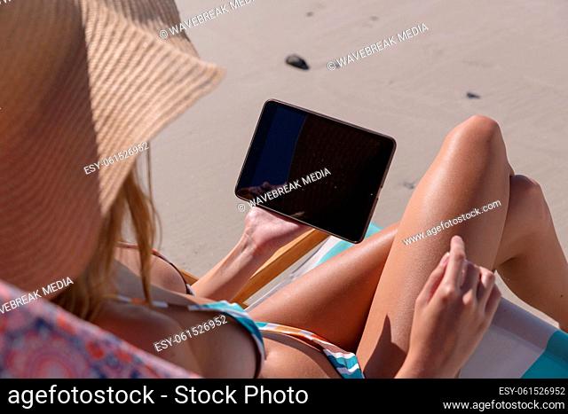 Mid section of caucasian woman using digital tablet while sitting on deck chair at the beach
