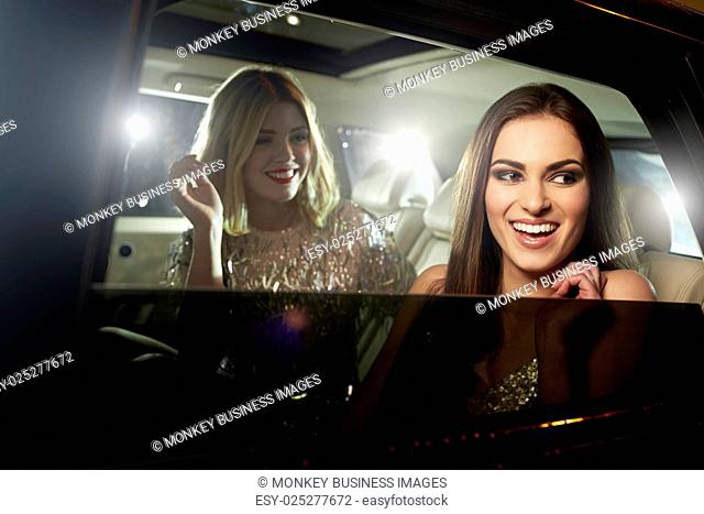 Two glamorous women laughing in the back of a limousine