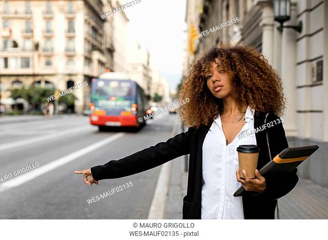 Young woman with laptop bag and coffee to go in the city, hailing a taxi