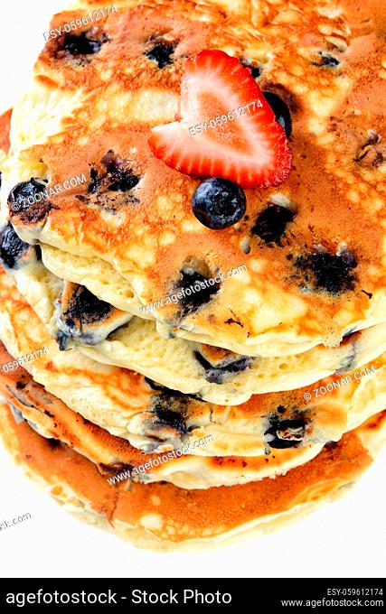 Closeup of a stack of fresh homemade blueberry pancakes topped with a strawberry on white plate and rustic wood table