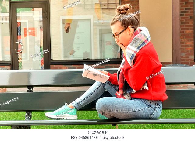 Asian girl sits on a bench and reads a book