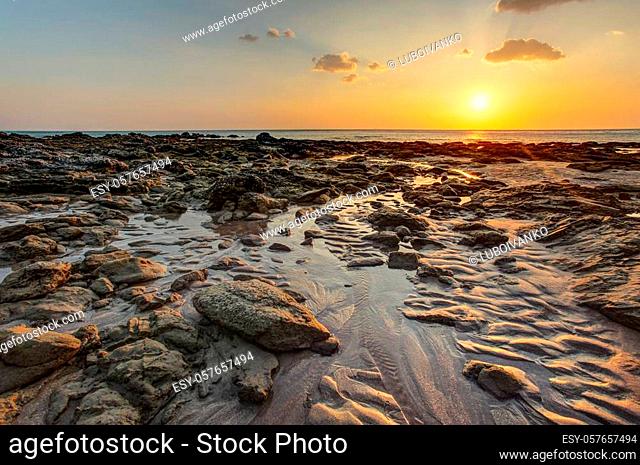 Beach in golden sunset light during low tide showing sand formations and wet stones not covered by the sea. Kantiang Bay, Ko Lanta, Thailand