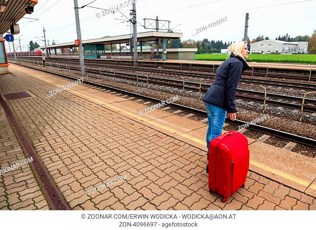Eine junge Frau mit Koffer wartet auf dem Bahnsteig eines Bahnhofes auf ihren Zug. Zugverspätungen