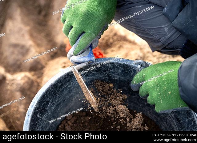 PRODUCTION - 18 October 2023, Bavaria, Friesen: Earth falls from a trowel into a bucket. Volunteers from the Kronach Archaeological Working Group uncover stone...
