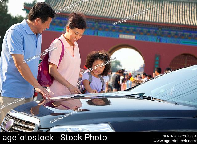 Grandparents and granddaughter standing next to the car and looking at the map