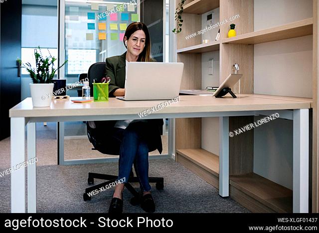 Concentrated female entrepreneur working on laptop while sitting at desk in office