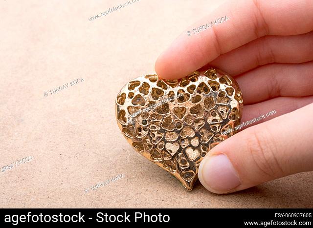 Heart shaped gold color metal object in hand