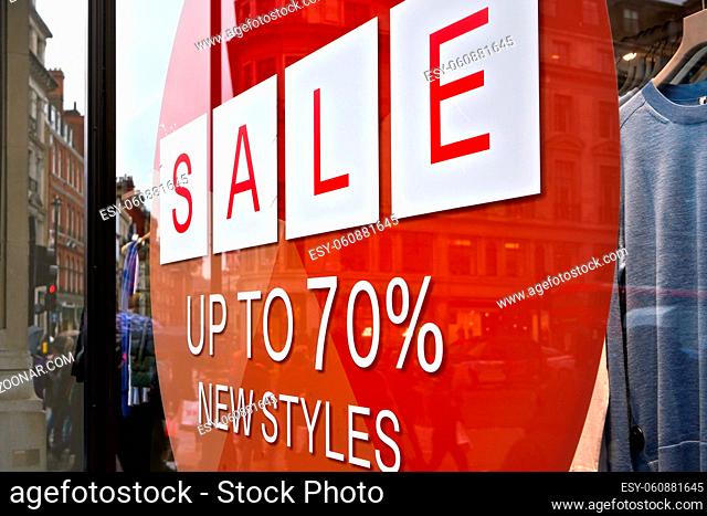 Sale up to seventy percent new styles sign - white letters in red circle - on glass window of clothes shop