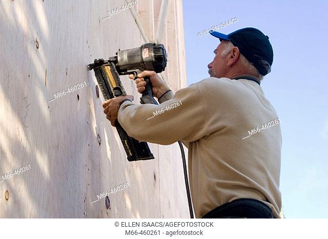 Carpenter shooting nails into plywood siding of a building under construction