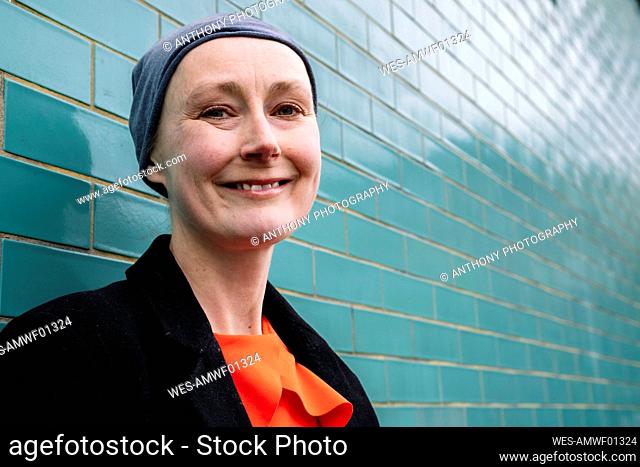 Smiling cancer patient wearing headscarf by brick wall