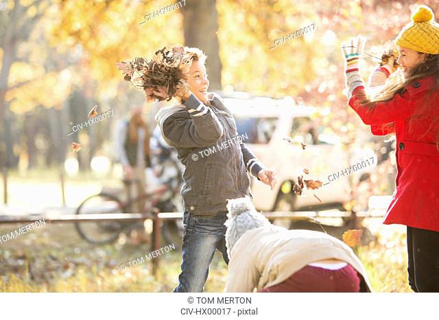 Boy throwing autumn leaves at girl in park