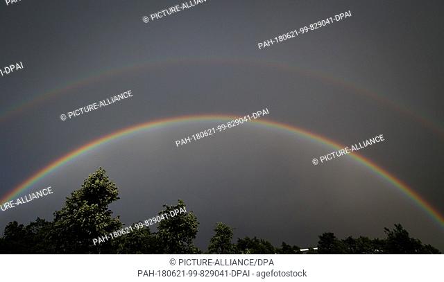 21 June 2018, Halle, Germany: A double rainbow can be seen beyond trees against the darkening horizon. Photo: Friso Gentsch/dpa