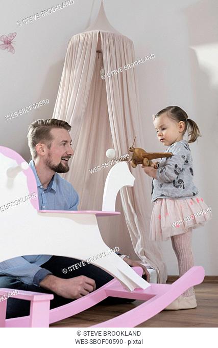 Father playing with toddler daughter in her nursery