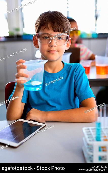 Portrait of caucasian boy holding a beaker filled with chemical in science class at laboratory