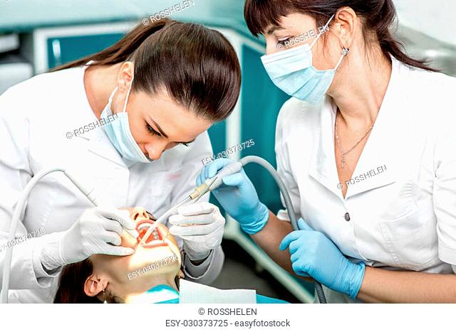 Dentist and nurse making professional teeth cleaning female young patient at the dental office