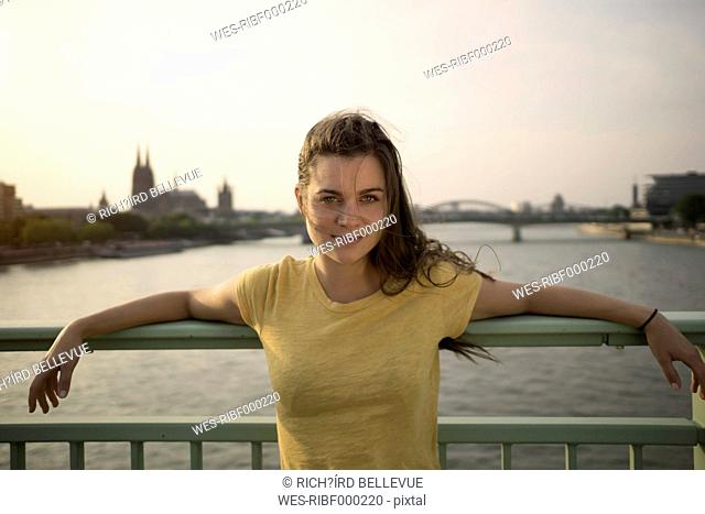 Germany, Cologne, portrait of young woman standing on Rhine bridge at evening twilight
