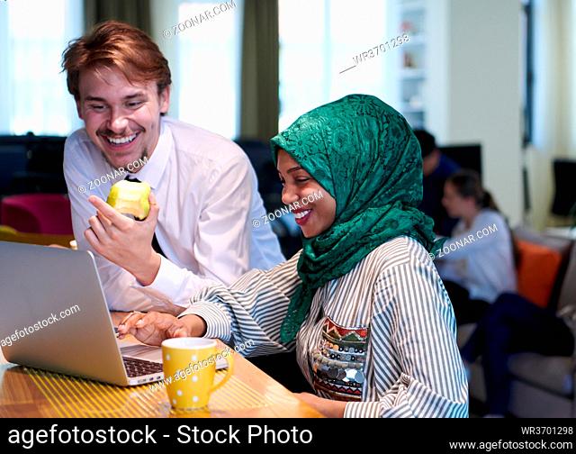 international multicultural business team.man eating apple african muslim woman wearing green hijab drinking tea while working together on laptop computer in...