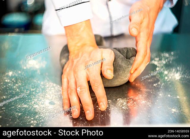 The chef's hand making dough for traditional italian pasta on a kitchen table