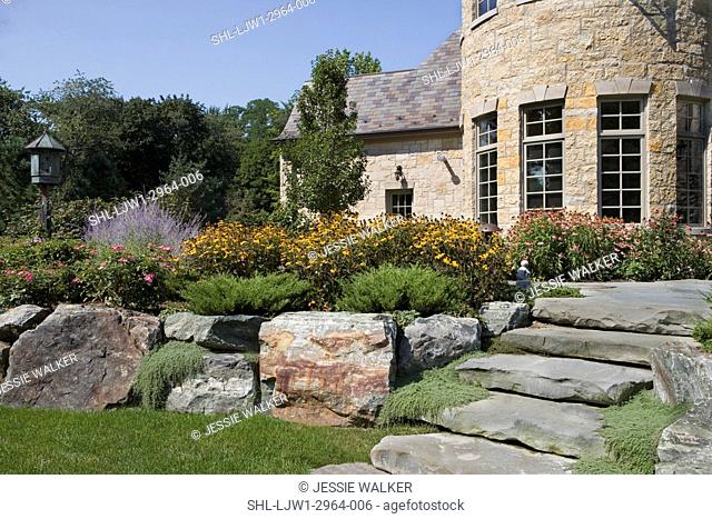 PATIOS: Backyard of French Normandy home, limestone patio and steps, less lawn and no path showing, stone steps lead to raised flower border and patio along...