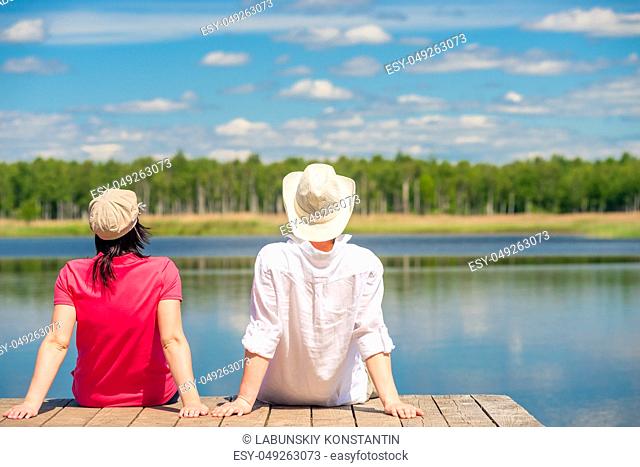 a loving couple enjoying a beautiful lake sitting on a wooden pier