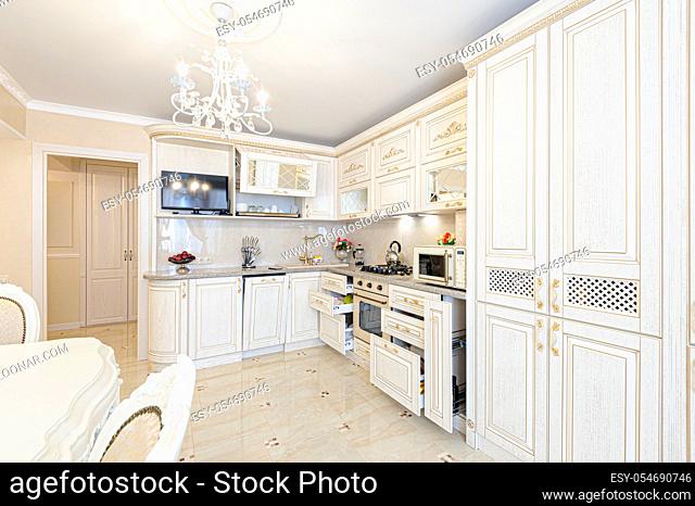 Luxury modern beige and cream colored kitchen in modern classic style. Some drawers are open