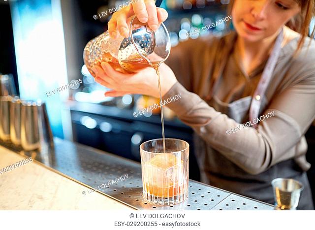 alcohol drinks, people and luxury concept - woman bartender with glass and jug preparing cocktail at bar