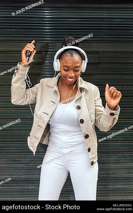 Woman dancing while listening music through headphones in front of shutter