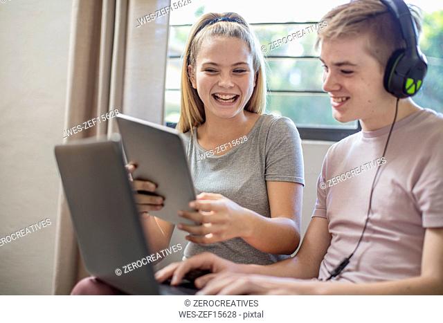 Happy boy and teenage girl with tablet, laptop and headphones