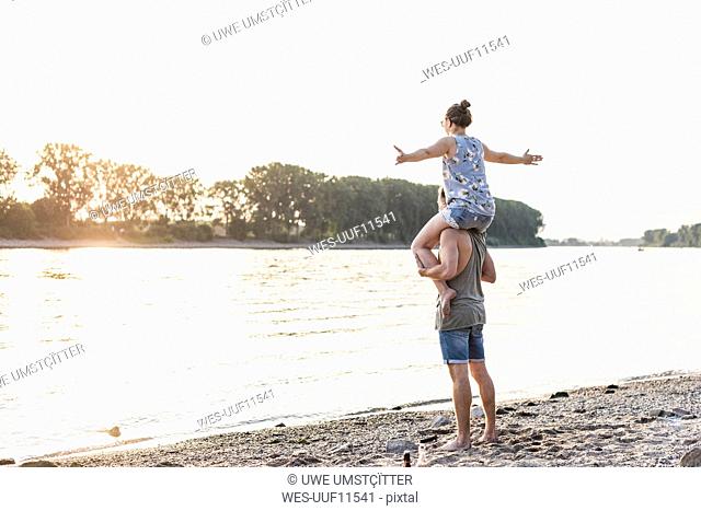 Young man carrying girlfriend on shoulders at the riverbank